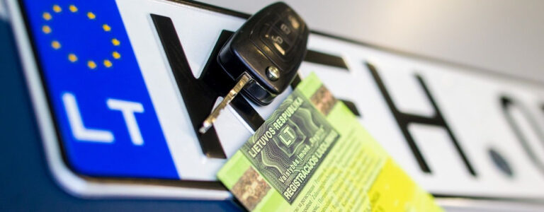 Stambiu planu matoma automobilio numerio lentelė su ES vėliava ir „LT“ žyma. Ant lentelės padėtas automobilio raktas, o po ja – dalinai matomas žalias dokumentas su tekstu lietuvių kalba: „Lietuvos Respublika“ ir „Registracijos liudijimas“.