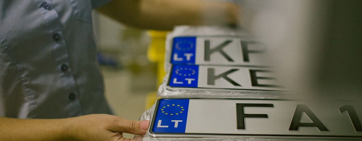 Asmuo laiko krūvą Europos Sąjungos numerių lentelių su mėlynu ES ženklu ir „LT“ žyma. Matomi numeriai: KP, KE, FA1.