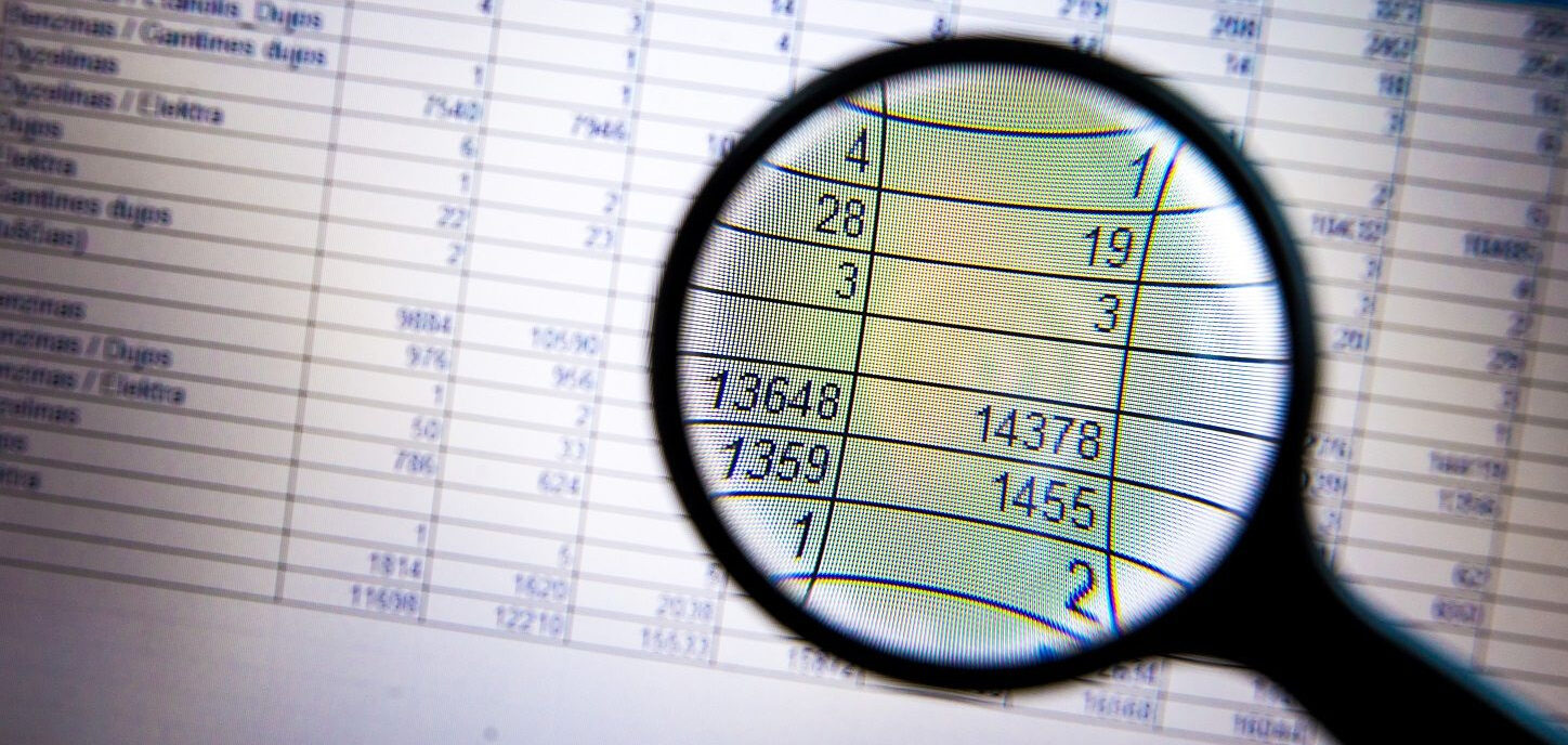 Padidinamasis stiklas sufokusuotas į skaičių lentelę, kurioje matomi tokie skaičiai kaip: 4, 1; 28, 19; 3, 3; 73648, 14378; 7359, 1455; 1, 2.