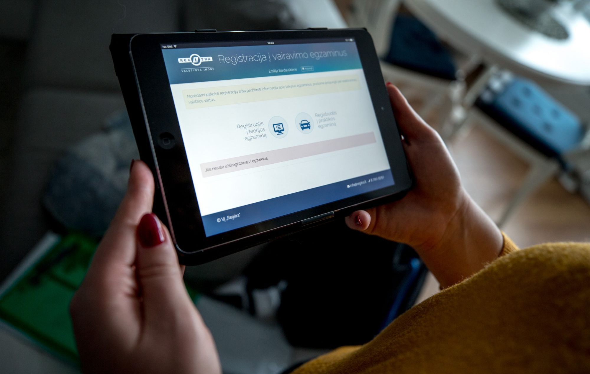 Asmuo laiko planšetę, kurios ekrane rodoma svetainė su vairavimo egzaminų registracijos galimybėmis.