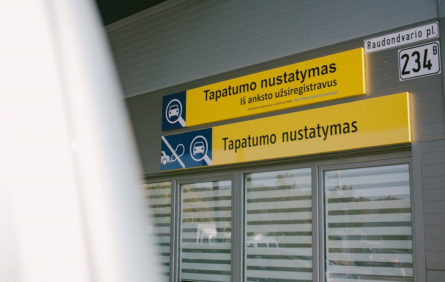 Pastatas su dviem geltonais informaciniais ženklais apie tapatumo nustatymą ir gatvės ženklu „Raudondvario pl. 234B“
