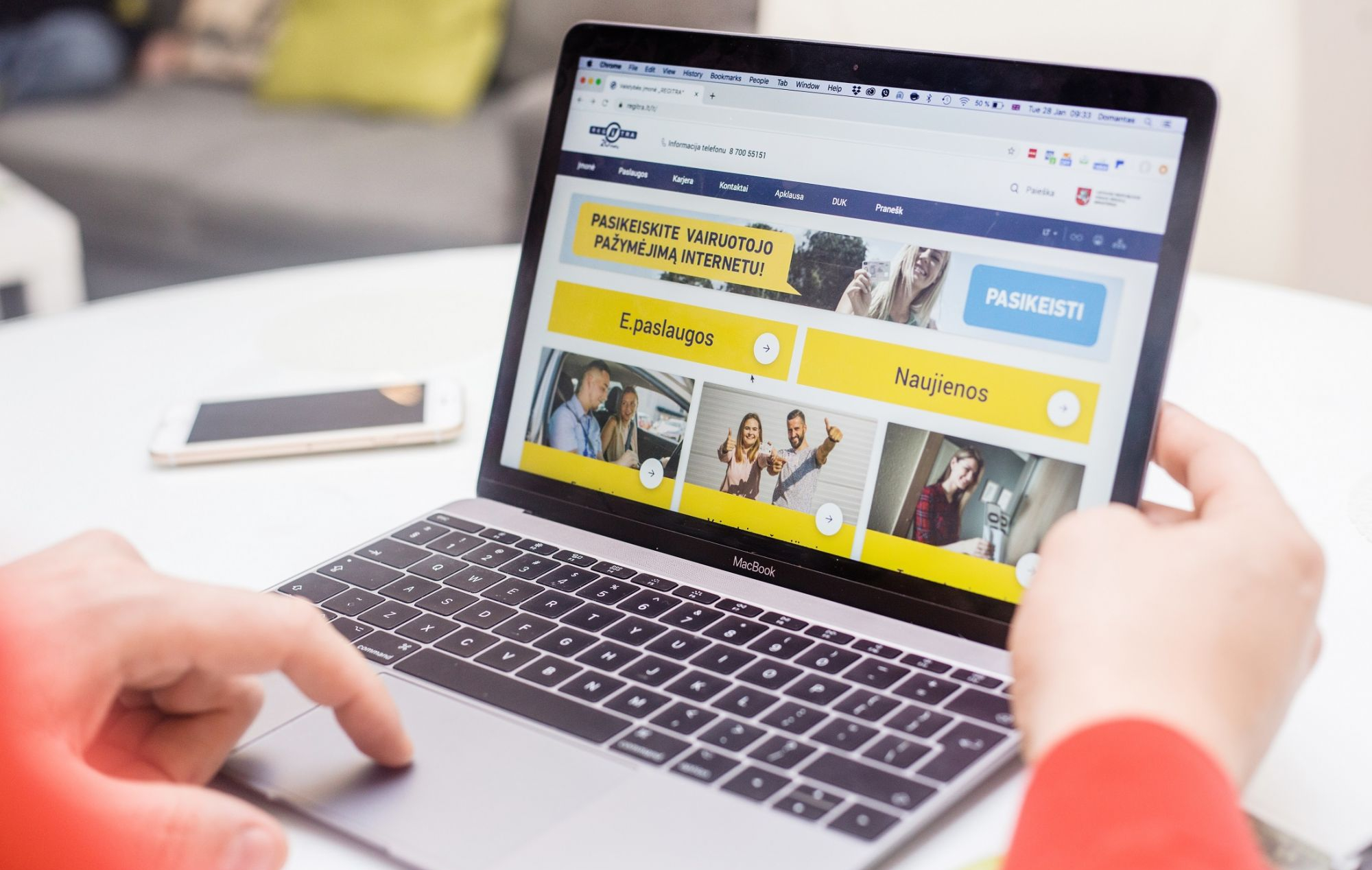 Nuotraukoje matomas žmogus, naudojantis „MacBook“ nešiojamąjį kompiuterį. Ekrane atidaryta svetainė lietuvių kalba, kurioje matyti tokie tekstai kaip: „PASIKEISKITE VAIRUOTOJO PAŽYMĖJIMĄ INTERNETU!“ „E.paslaugos“ „Naujienos“