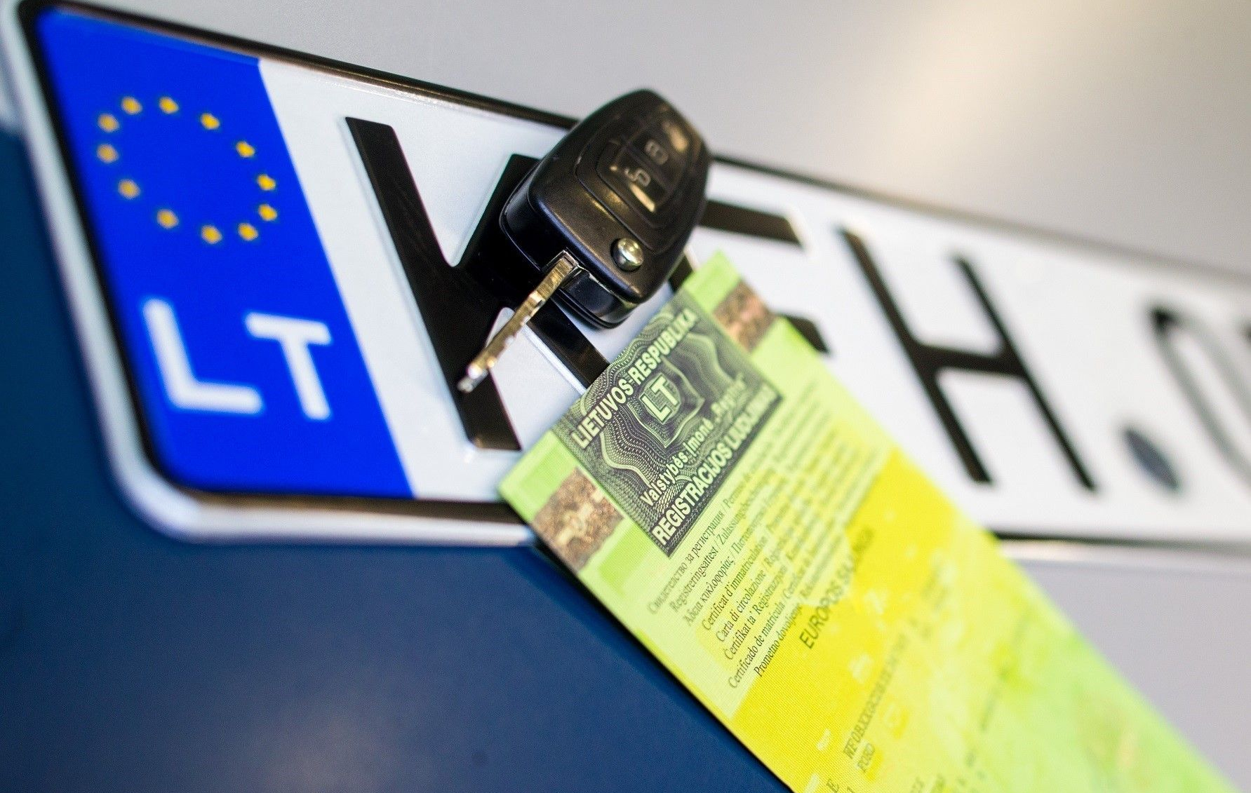 Automobilio valstybinis numeris su įstatyta raktu, laikantis žalią transporto priemonės registracijos liudijimą.