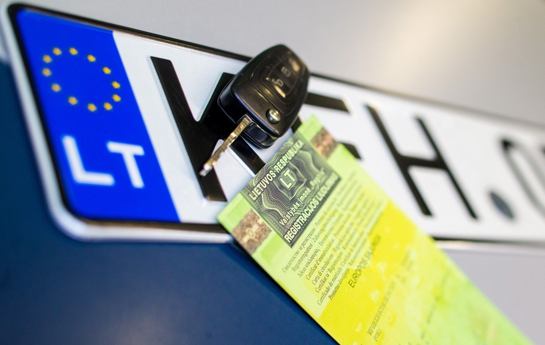Automobilio valstybinis numeris su įstatyta raktu, laikantis žalią transporto priemonės registracijos liudijimą.