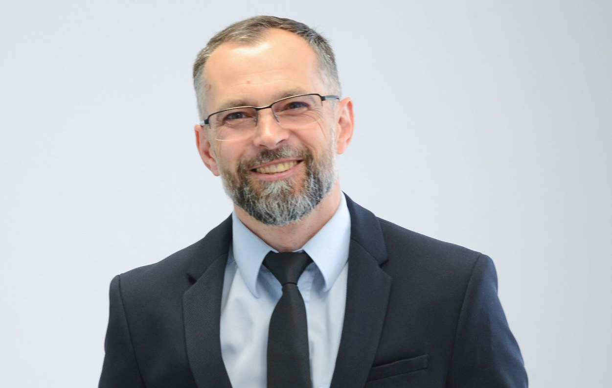 Vyras su akiniais ir kostiumu šypsosi