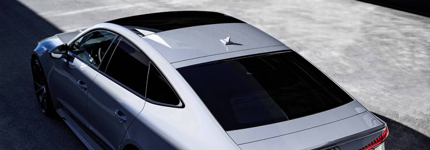 Sidabrinis automobilis, matomas iš viršaus, su tamsintais langais ir stogo antena, pastatytas ant betoninio paviršiaus.