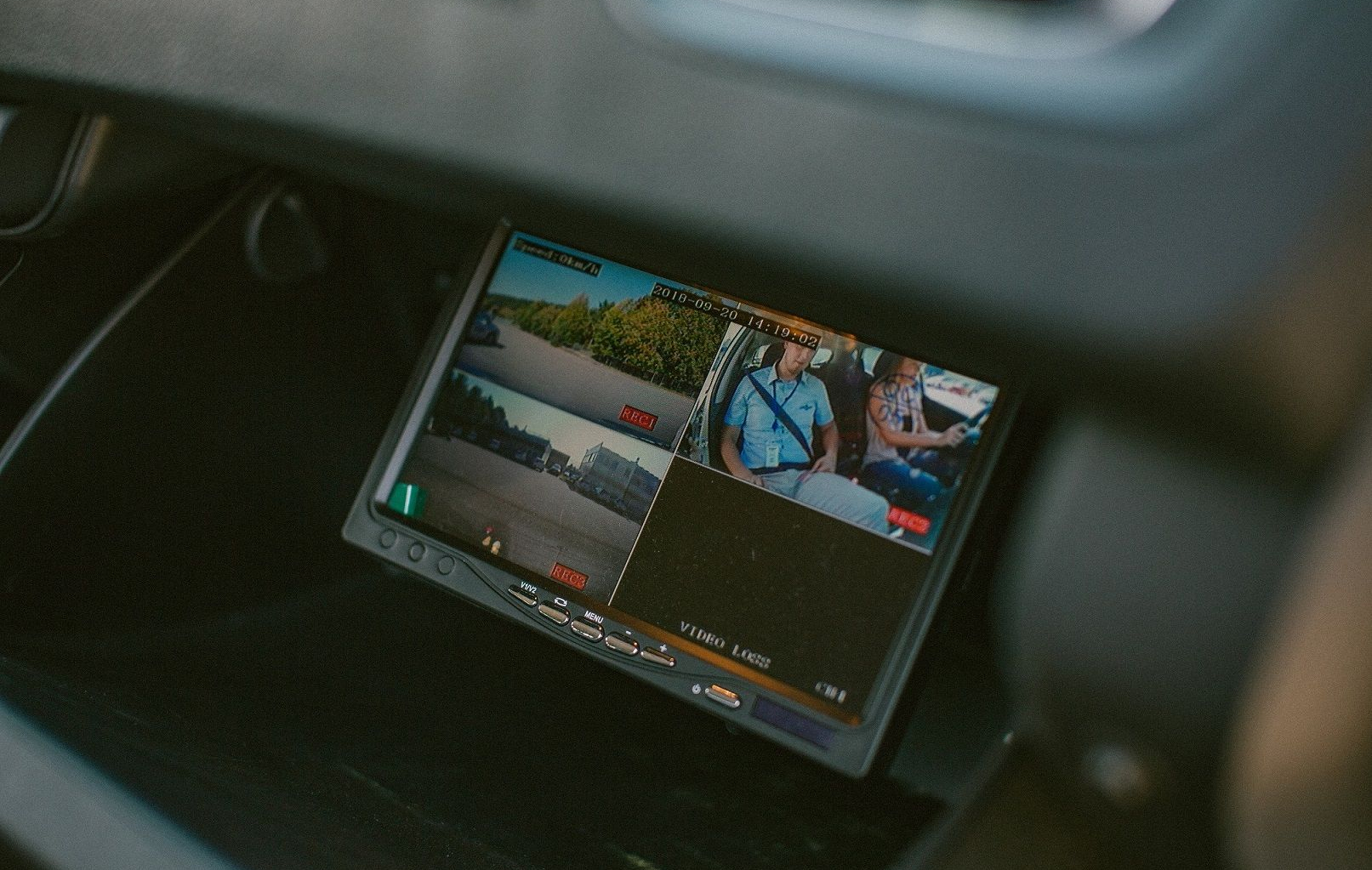 Transporto priemonės stebėjimo monitorius su keturiais vaizdo kanalais, rodančiais kelią ir keleivius, vienas kanalas tuščias.