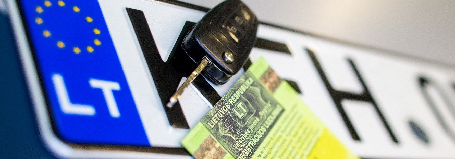 Automobilio valstybinis numeris su įstatyta raktu, laikantis žalią transporto priemonės registracijos liudijimą.