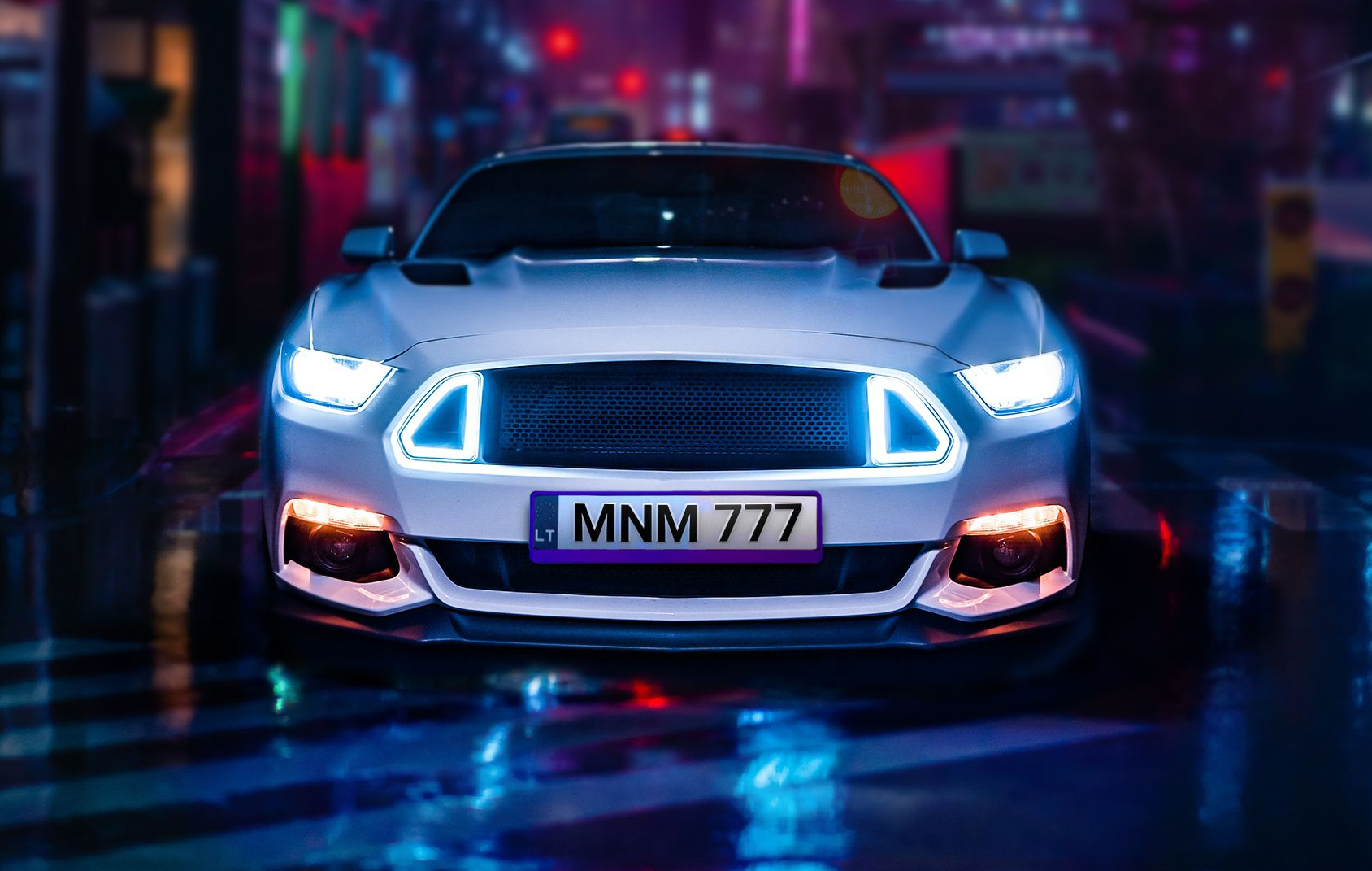 Baltas sportinis automobilis su įjungtais žibintais, stovintis šlapioje gatvėje naktį. Numeris – „LT MNM 777“.