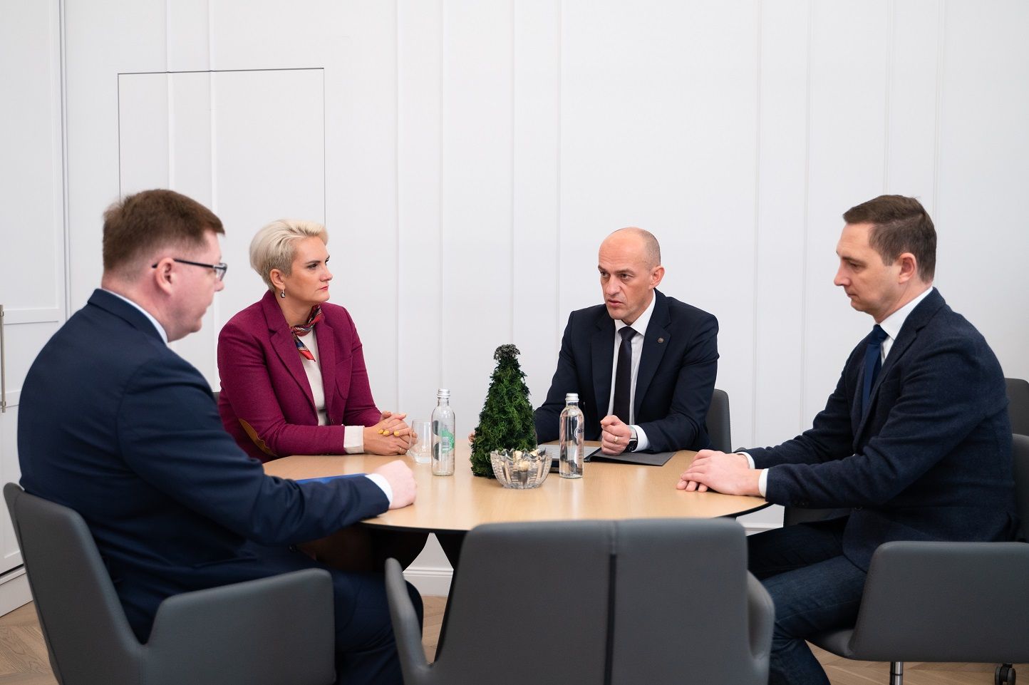 trys kostiumuoti vyrai ir moteris susėdę aplink stalą