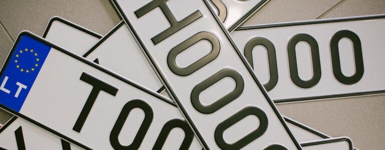 Europos stiliaus automobilio numerių kolekcija, persidengiančios lietuviškos numerių lentelės su juodais simboliais baltame fone ir mėlyna ES vėliavos juosta kairėje.