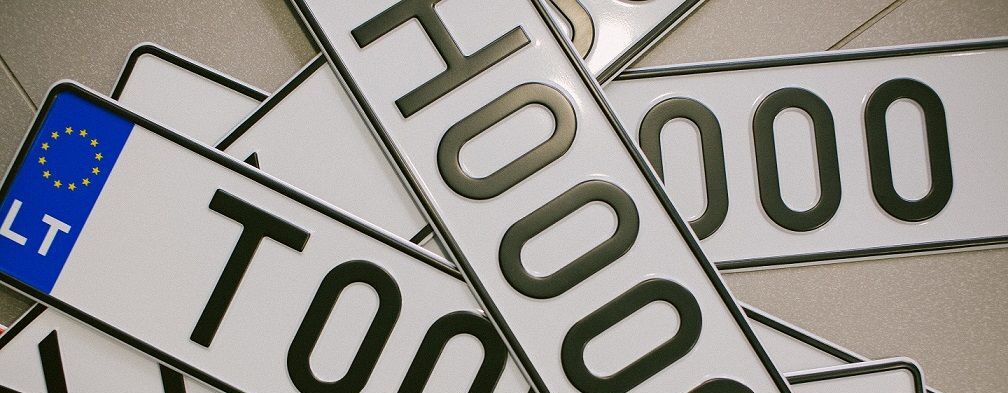 Europos stiliaus automobilio numerių kolekcija, persidengiančios lietuviškos numerių lentelės su juodais simboliais baltame fone ir mėlyna ES vėliavos juosta kairėje.