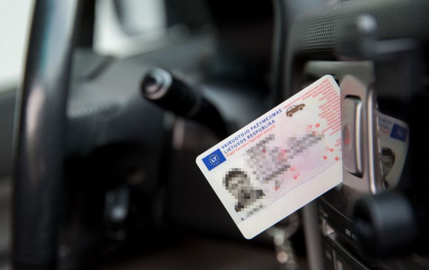 Lietuvos vairuotojo pažymėjimas padėtas automobilio viduje, šalia prietaisų skydelio. Matomas užrašas „VAIRUOTOJO PAŽYMĖJIMAS LIETUVOS RESPUBLIKA“, kiti duomenys neryškūs.
