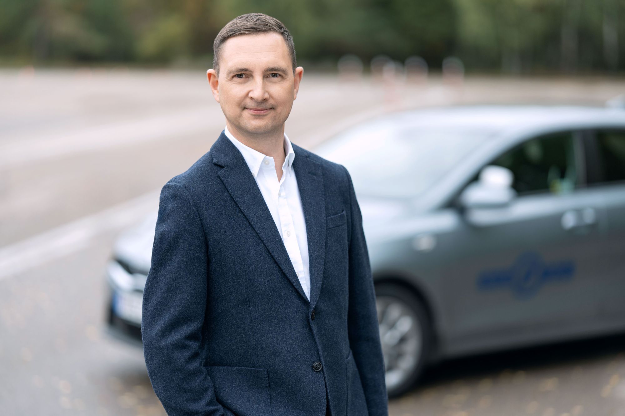 Vyras su mėlyny kostiumu prie Regitros automobilio.