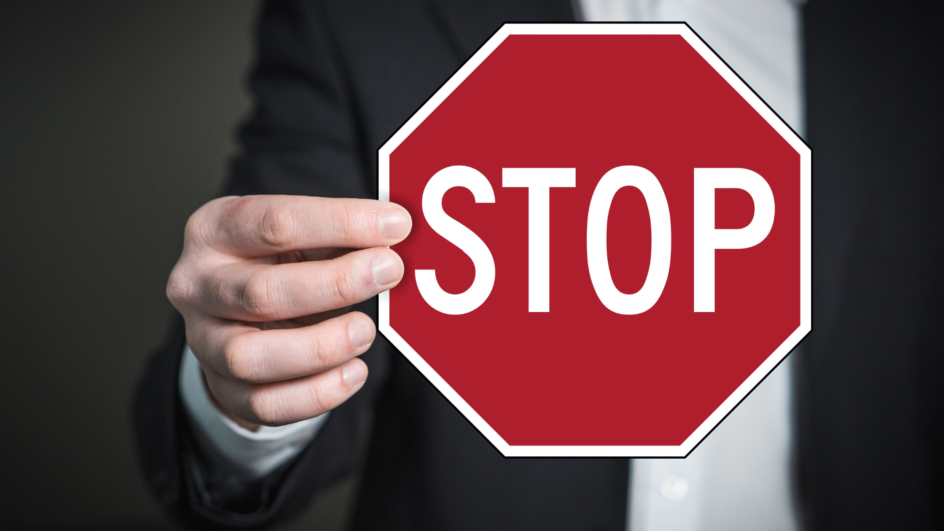Asmuo laiko raudoną aštuonkampį ženklą su baltu užrašu „STOP“.
