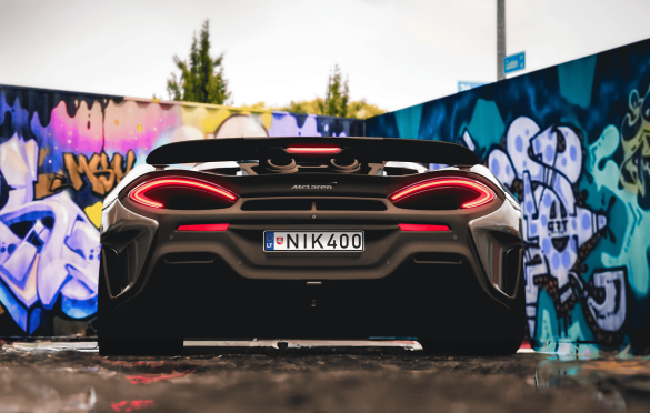 McLaren sportinis automobilis su numeriais „NIK400“, stovintis prieš spalvingą grafičiais išmargintą sieną, kurioje dominuoja mėlynos, violetinės ir geltonos spalvos.
