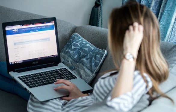Asmuo sėdi ant sofos ir naudojasi ASUS nešiojamuoju kompiuteriu, kurio ekrane matoma svetainė su pavadinimu „Registracija užsiėmimų registracijai“ ir formos laukais.