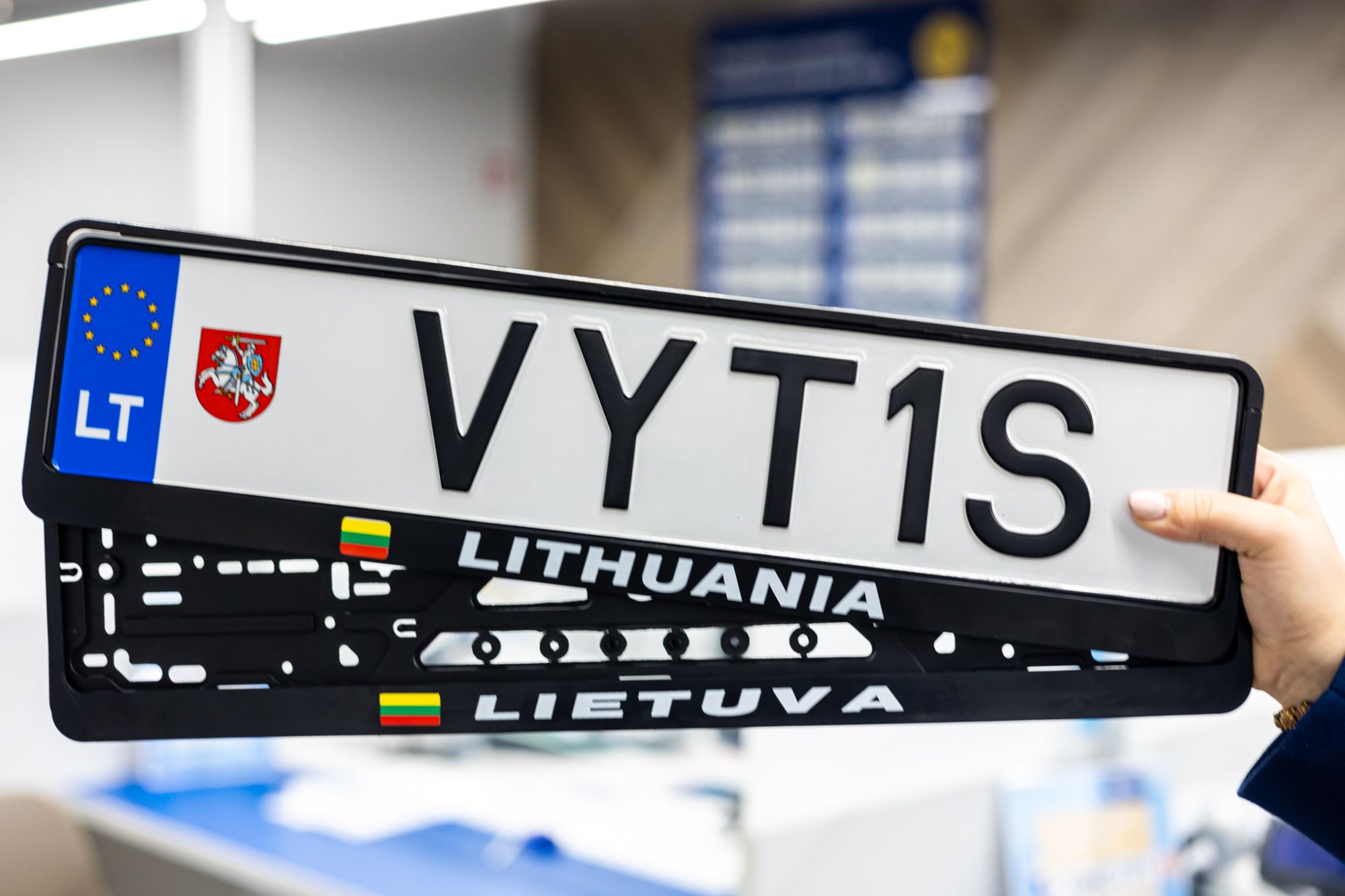 Lietuviški automobilio valstybiniai numeriai „VYT1S“ su ES vėliava ir „LT“ žymėjimu kairėje; po numeriais – du juodi rėmeliai su užrašais „LITHUANIA“ ir „LIETUVA“, abiejuose matomos mažos Lietuvos vėliavos.