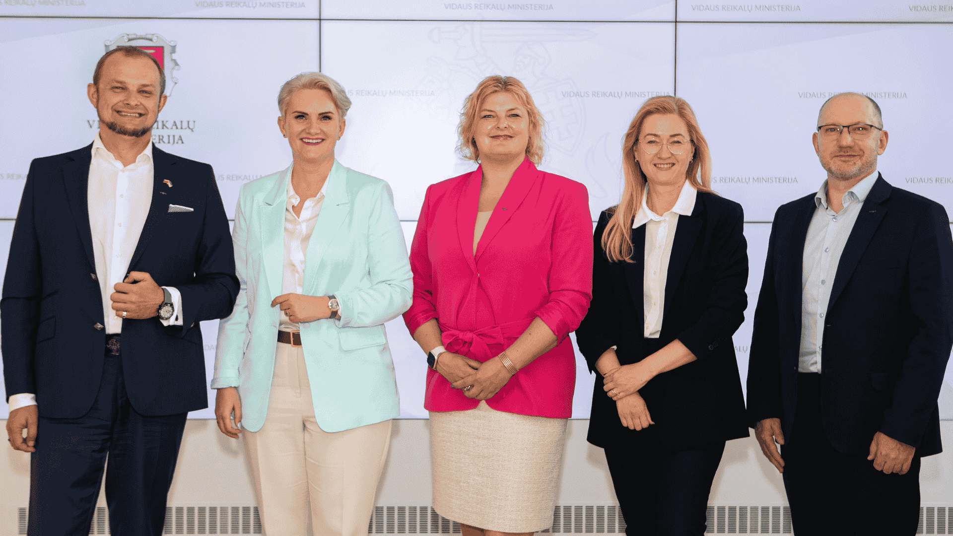 Penki asmenys stovi prieš foną su užrašais „Vilniaus miesto savivaldybė“ ir „Vilniaus miesto ministerija“; visi vilki oficialius drabužius.