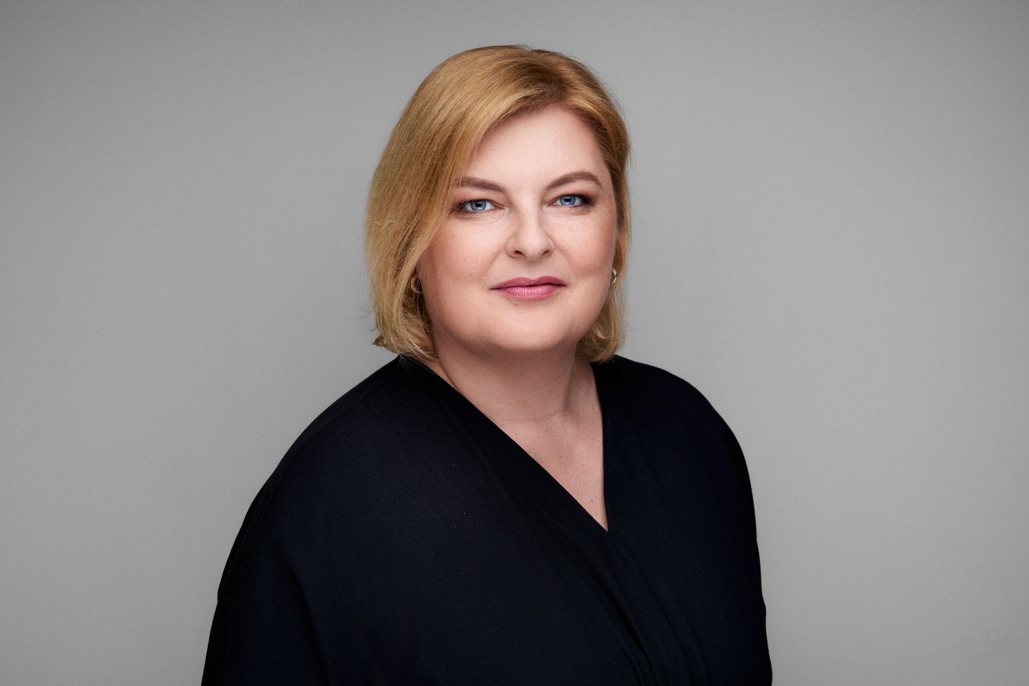 Asmuo trumpais šviesiais plaukais, vilkintis tamsios spalvos viršutinį drabužį.