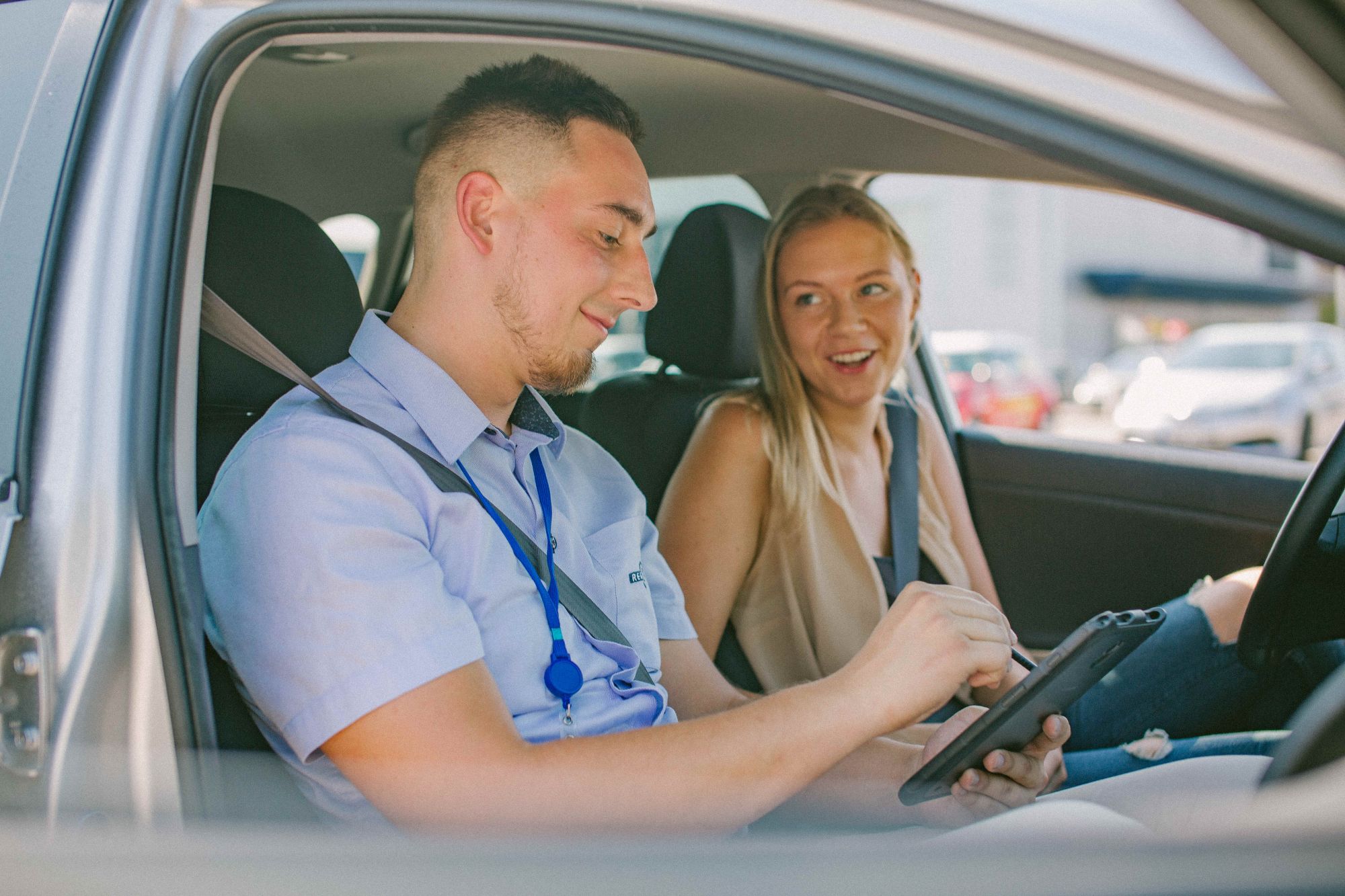 Du žmonės sėdi automobilyje. Vienas jų laiko planšetę, o kitas žiūri į ją. Abu asmenys yra su neryškiais veidais privatumo sumetimais.
