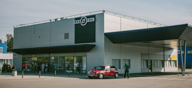 Pastatas su užrašu „REGITRA“ ir automobilių stovėjimo aikštelė prie jo.