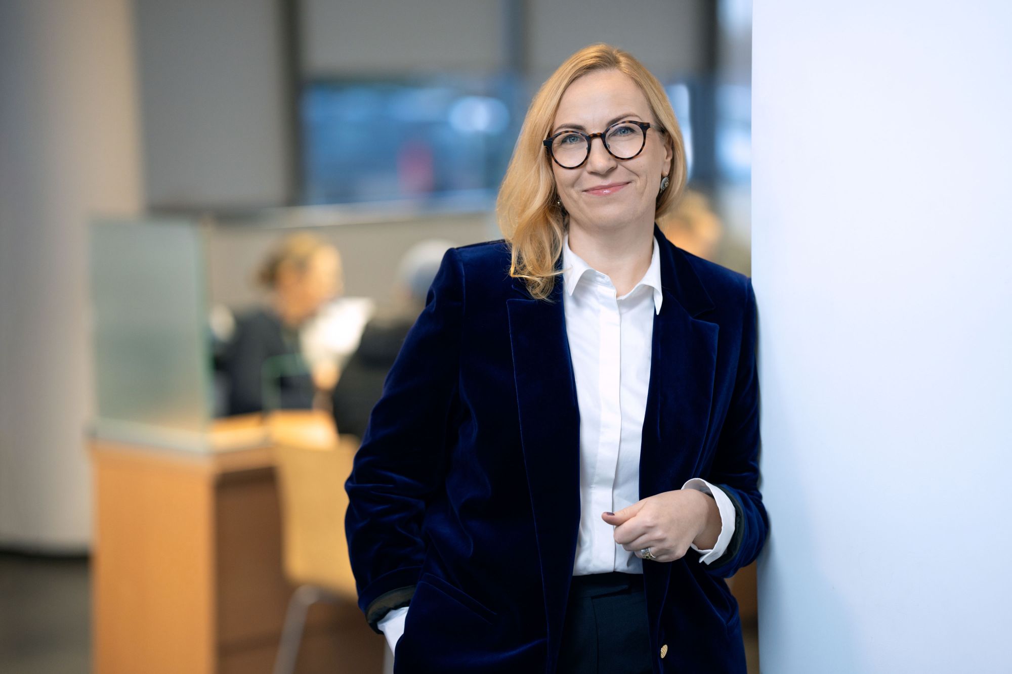 Moteris su tamsiai mėlynu kostiumėliu ir akiniais