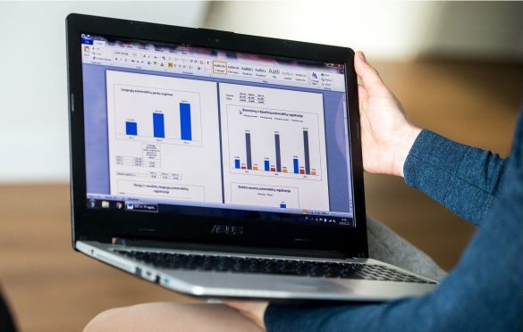 Žmogaus rankos laiko nešiojąmą kompiuterį, kuriame matyti diagramos