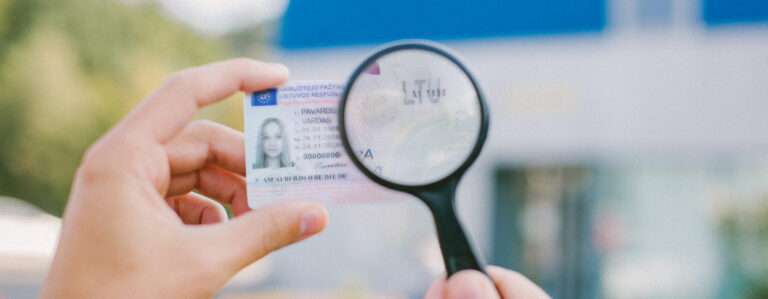Asmuo laiko padidinamąjį stiklą virš Lietuvos asmens dokumento, išryškinant tekstą „LTU“ ir skaičius