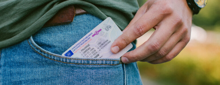 Asmuo įdeda arba išima Lietuvos vairuotojo pažymėjimą iš mėlynų džinsų priekinės kišenės