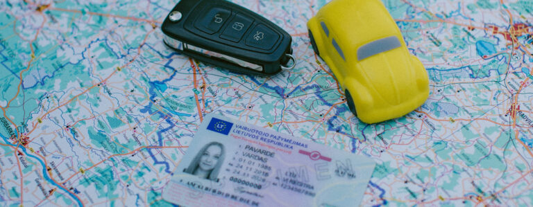 Žemėlapio fone padėtas automobilio raktas, geltonas žaislinis automobilis ir Lietuvos vairuotojo pažymėjimas