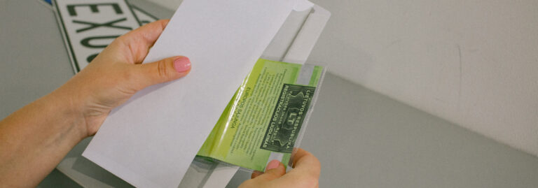 Rankos laiko voką ir įdeda arba išima žalią dokumentą su tekstu „Lietuvos Respublikos registracijos liudijimas