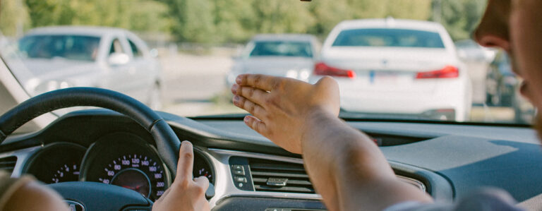 Vairavimo egzaminas automobilyje, egzaminuotojas ranka rodo kryptį