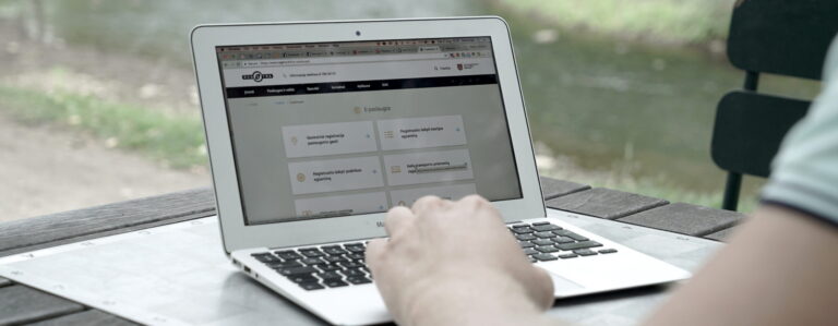 Šioje nuotraukoje matomas asmuo, naudojantis MacBook Air nešiojamąjį kompiuterį. Ekrane atidaryta Regitros svetainė.