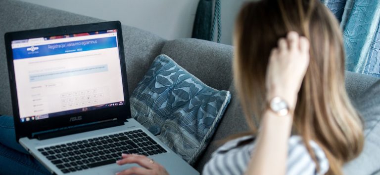 Mergina sėdi ant sofos namuose ir registruojasi į vairavimo egzaminą internetu