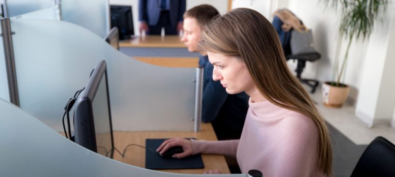 Du žmonės laiko teorijos vairavimo egzaminus kompiuteriuose atskirose darbo vietose su stiklinėmis pertvaromis Regitroje