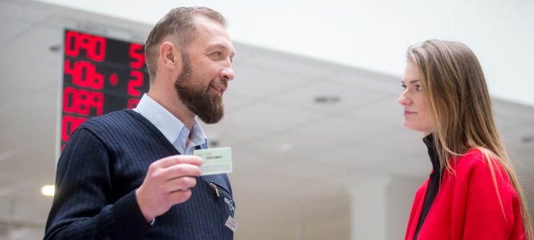 Du žmonės „Regitros“ patalpose, darbuotojas rankoje laiko kliento asmens dokumentą, klientas stovi šalia.