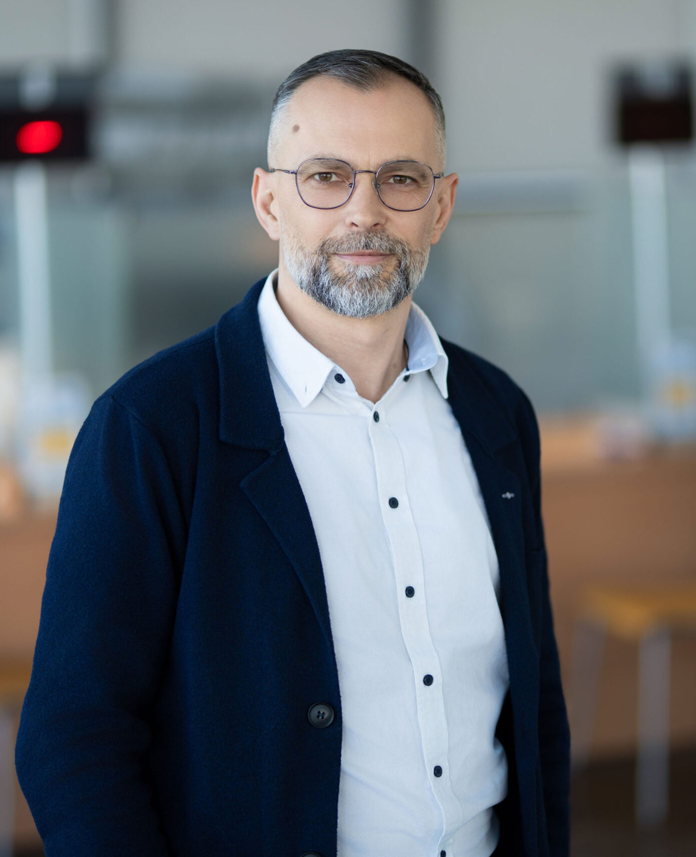 Vyras su akiniais, baltais marškiniais ir tamsiai mėlynu megztuku