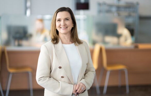 Moteris su kreminiu švarku šypsosi.