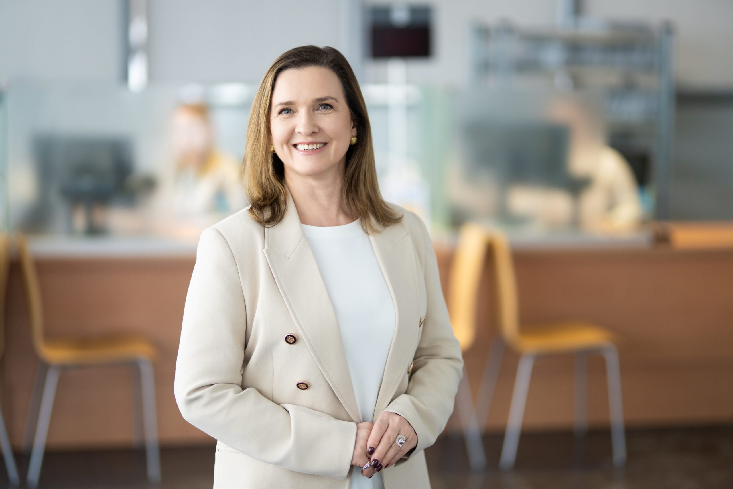 Moteris su kreminiu švarku šypsosi.