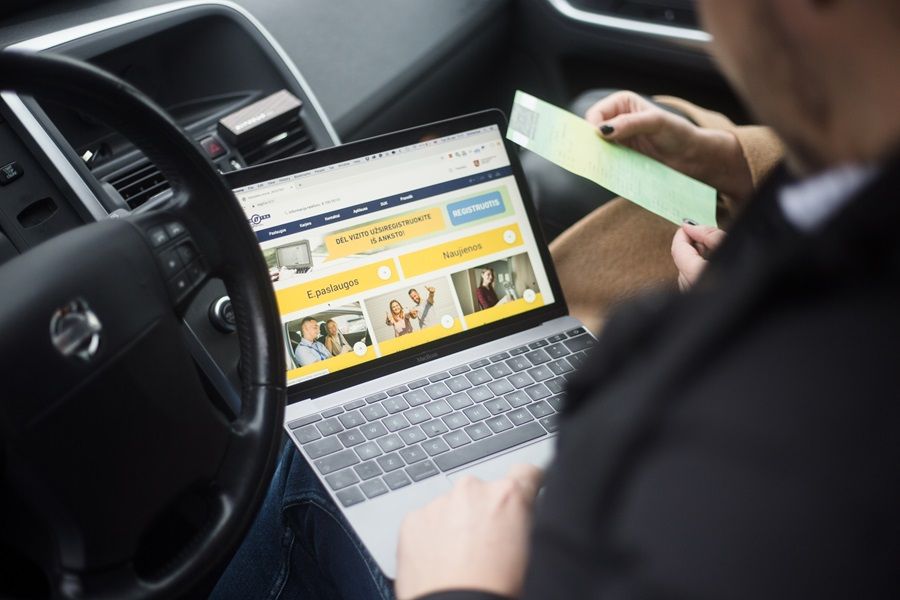 Žmogus sėdi automobilyje ir kompiuteryje užsakinėja elektronines paslaugas