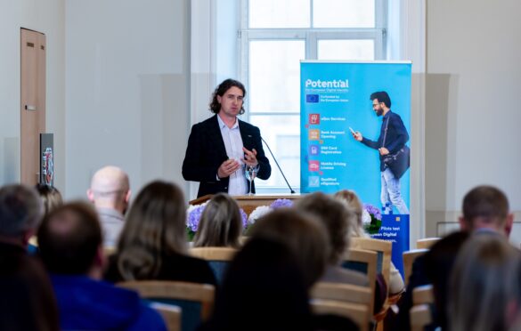 Vyras su švarku kalba prie tribūnos konferencijoje