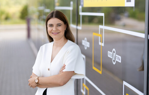 Moteris sukryžiavusi rankas stovi prie stiklinės sienos lauke