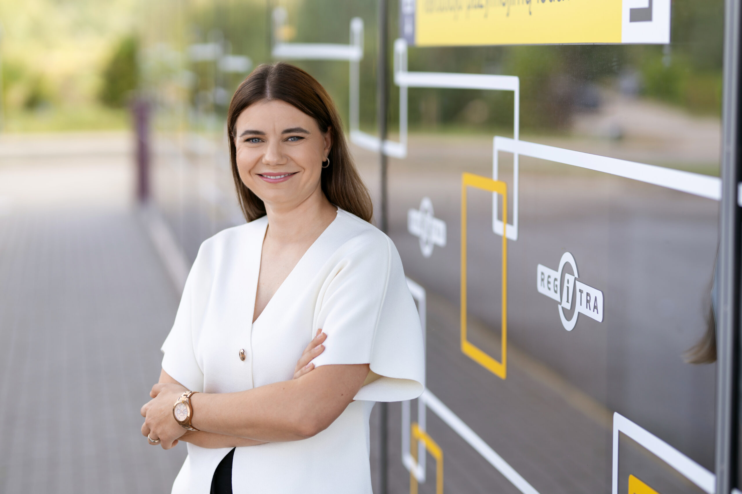 Moteris sukryžiavusi rankas stovi prie stiklinės sienos lauke