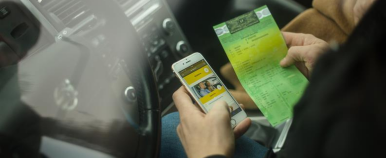 Asmuo rankose laiko išmanųjį telefoną su atidaryta Regitros programėle, o kitoje rankoje – automobilio registracijos liudijimas.