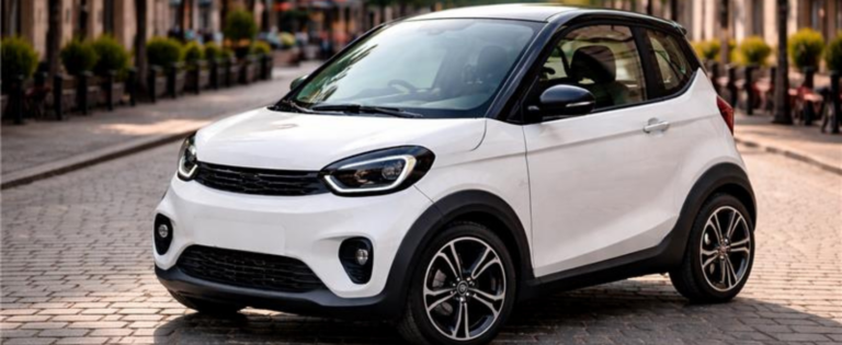 Balta kompaktiška miesto automobilio tipo transporto priemonė stovi ant grindinio miesto gatvėje; fonas šiek tiek neryškus, matyti pastatai ir želdiniai.